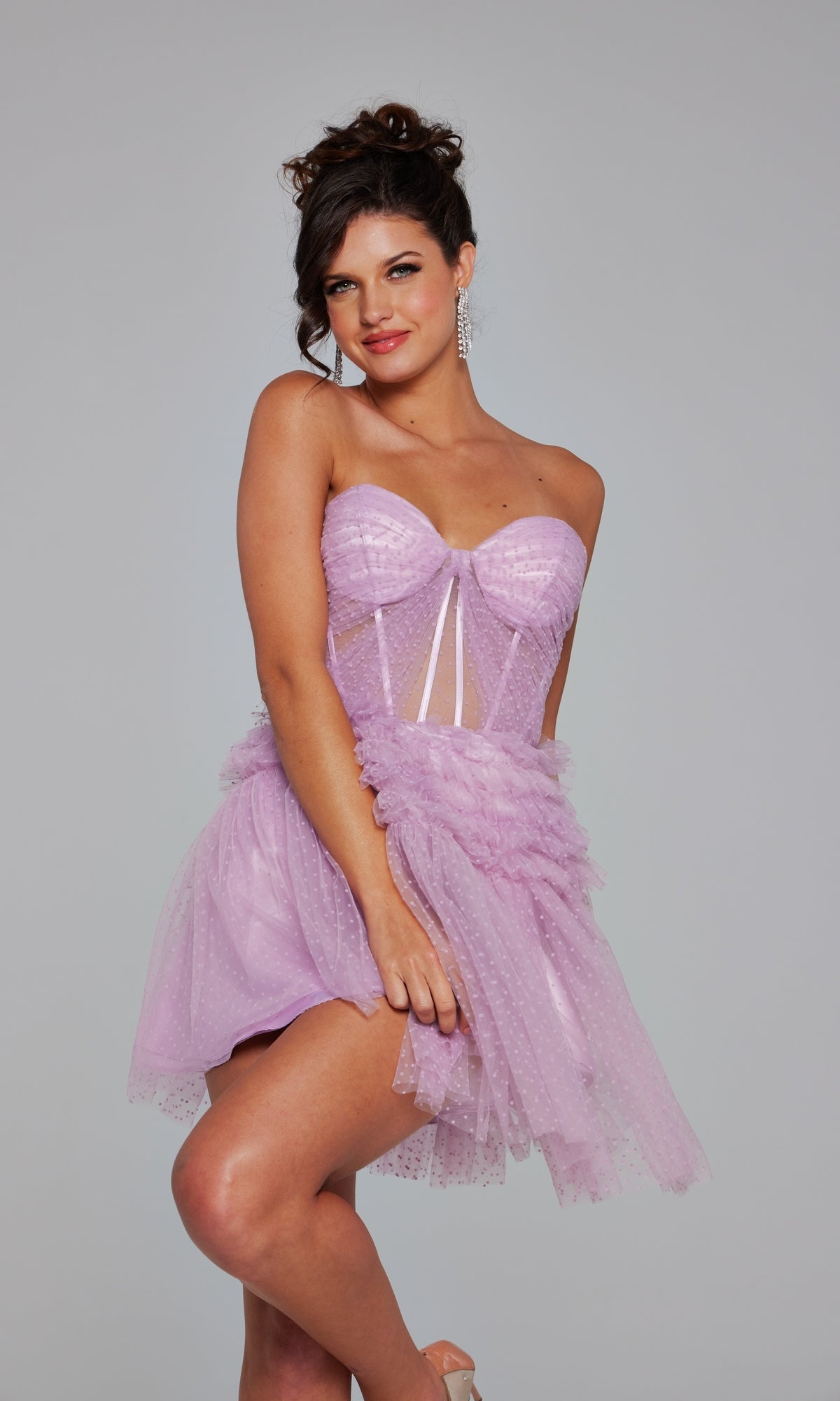 A woman poses in the Short Homecoming Dress 40467 by Jovani, a light purple strapless A-line dress with a sheer corset bodice, tulle accents, and polka dot texture, set against a plain gray background.